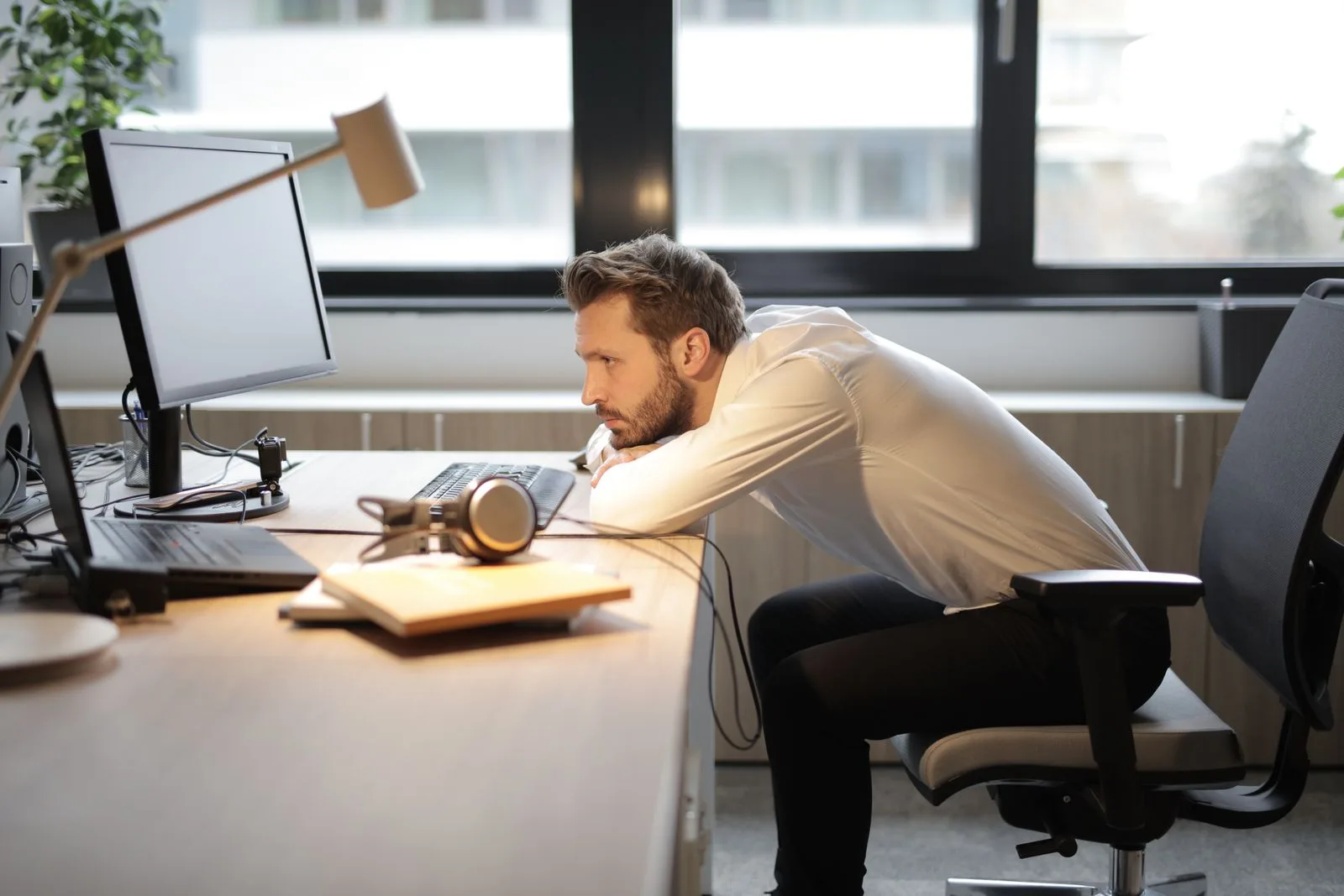 Colaborador curvado sobre a mesa, pescoço esticado em direção à tela do computador